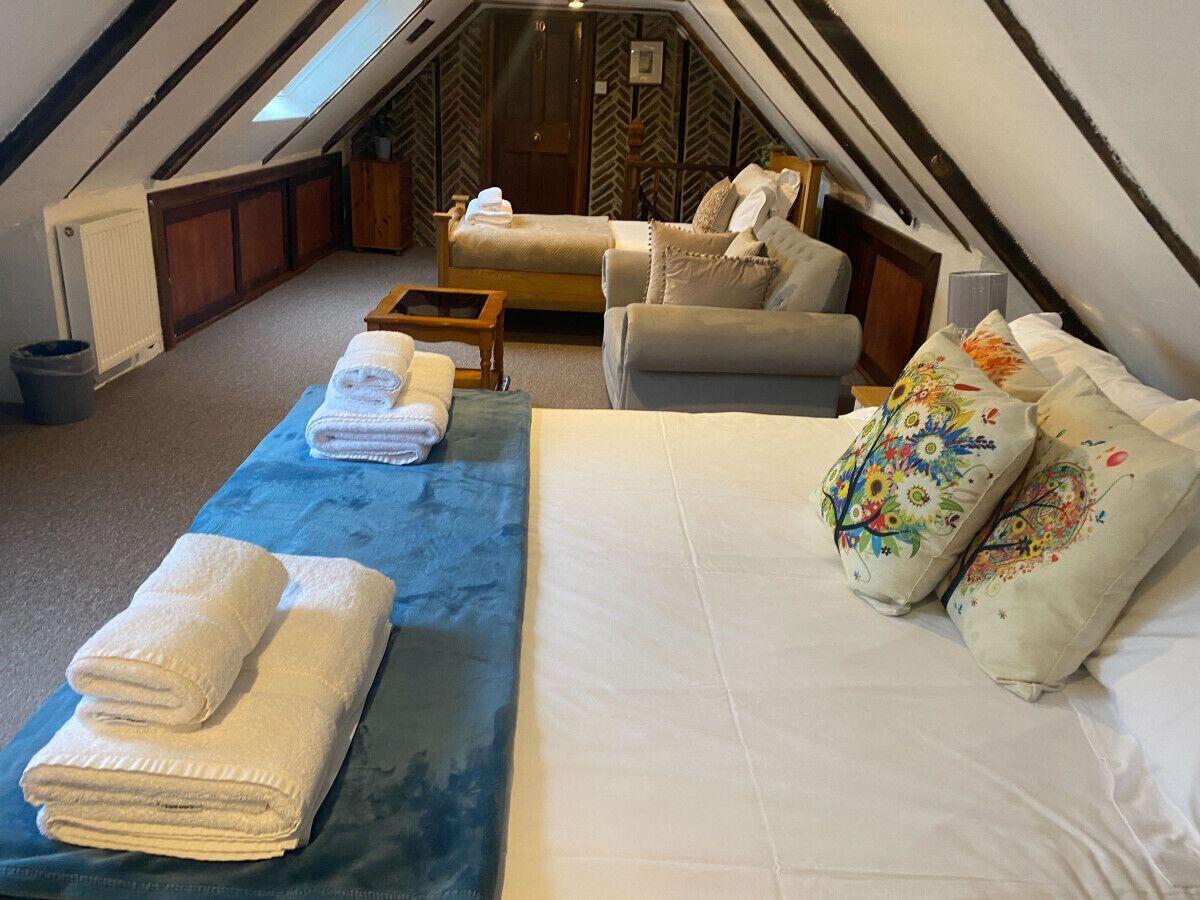 Un dormitorio acogedor en el ático con una cama grande, un sofá y una mesita pequeña. Hay toallas y almohadas decorativas sobre la cama.