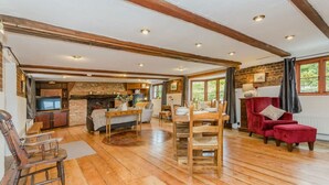 A spacious living area with wooden floors, a fireplace, a dining table set for four, and a red armchair.