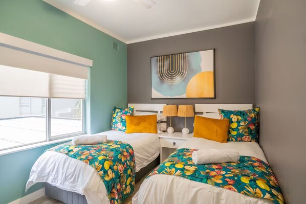 Quarto de hotel com duas camas, uma janela, um quadro e uma mesa de cabeceira.