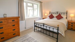 A bedroom with a bed, wooden dresser, two bedside tables with lamps, a window with curtains, and a radiator. - Tuliptree (Chesterfield)