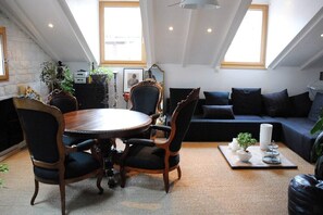 Un espace de vie de style loft comprenant un coin repas, un canapé de couleur sombre et une grande fenêtre laissant entrer la lumière naturelle.