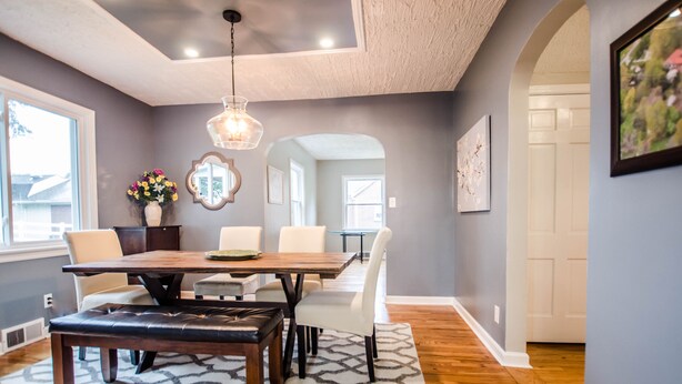 A dining area with a wooden table, white chairs, a patterned rug, and a hanging light fixture.