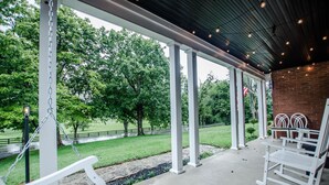A covered patio with white rocking chairs, a swing, and a brick wall.