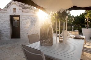 Un'area pranzo all'aperto con un edificio in pietra, un tavolo apparecchiato con stoviglie bianche e un'elegante composizione floreale.