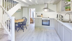 Une cuisine moderne avec des meubles blancs, un four encastré et un coin repas comprenant une table et des chaises en bois.