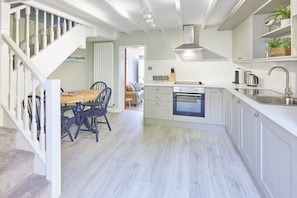 Une cuisine moderne avec des meubles blancs, un four encastré et un coin repas comprenant une table et des chaises en bois.