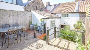 Une terrasse avec une table et des chaises, un petit bâtiment blanc avec un toit en tuiles et une clôture en bois.