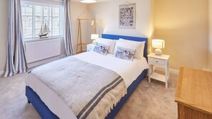 Une chambre à coucher comprenant un lit, des tables de chevet, une fenêtre avec des rideaux, un radiateur et une œuvre d’art accrochée au mur.