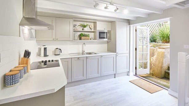 Une cuisine moderne avec des meubles blancs, un four à micro-ondes encastré et une grande fenêtre.