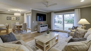 A spacious living room with a flat-screen TV, a ceiling fan, and a large sliding glass door leading to a backyard. - Sunset Rentals | Heritage Villas 2292 (Hilton Head Island)