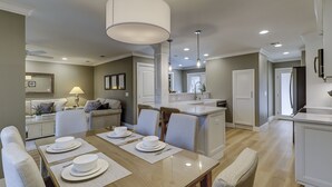 A modern kitchen with a central island, dining table with chairs, and a living area with a sofa and lamp. - Sunset Rentals | Heritage Villas 2292 (Hilton Head Island)