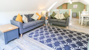 A cozy living room with two grey sofas, a patterned rug, and a dining area with a table and chairs. - Old Wood Coach House (Lincoln)