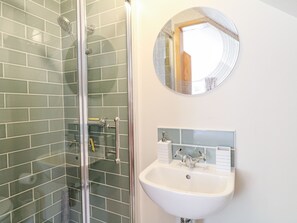Un baño con cabina de ducha de vidrio, un lavabo blanco con un espejo encima y pared de azulejos.