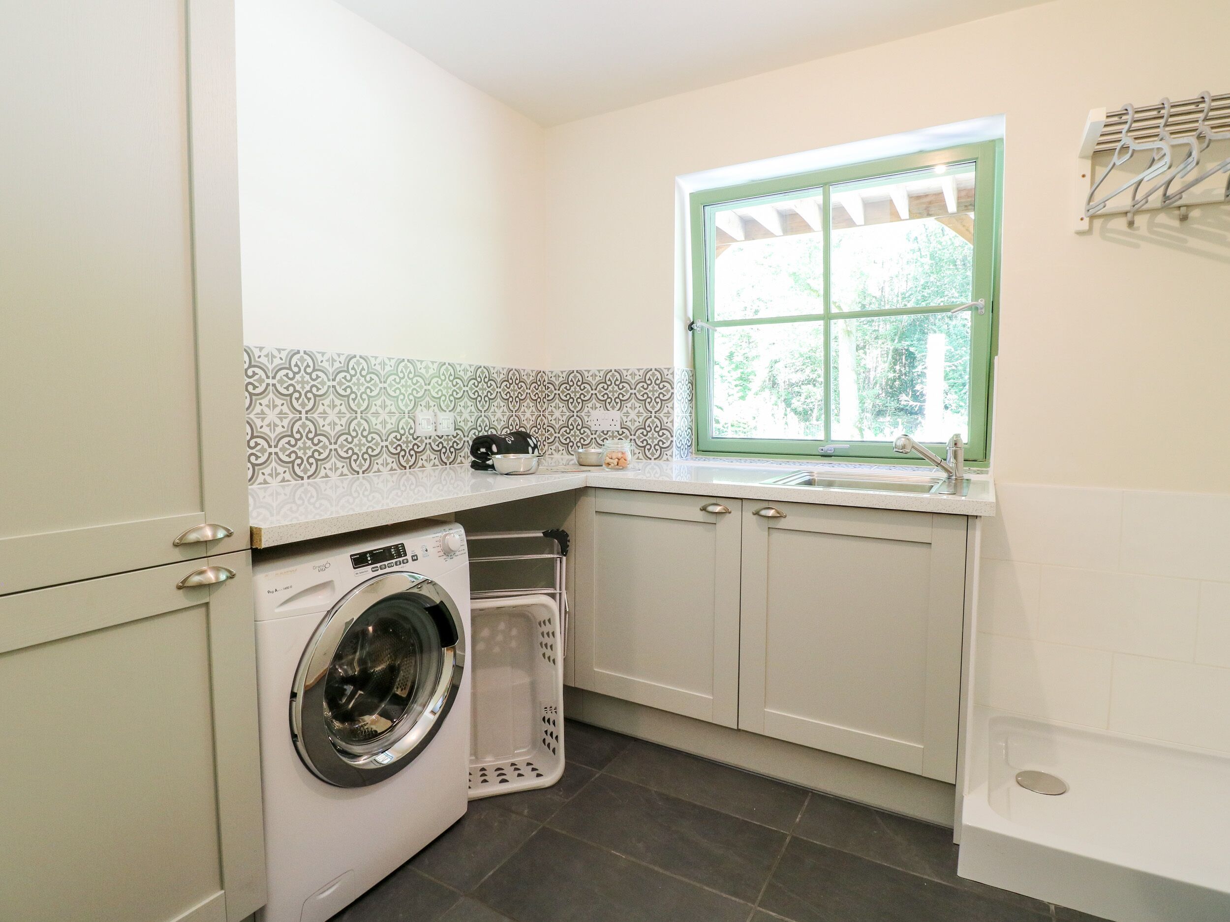 A compact kitchen with a built-in washing machine, a window with a view of greenery, and a tiled backsplash.