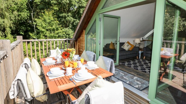 A wooden deck with a table set for breakfast, a sofa, and a glass door leading to a living area. - Old Wood Coach House (Lincoln)
