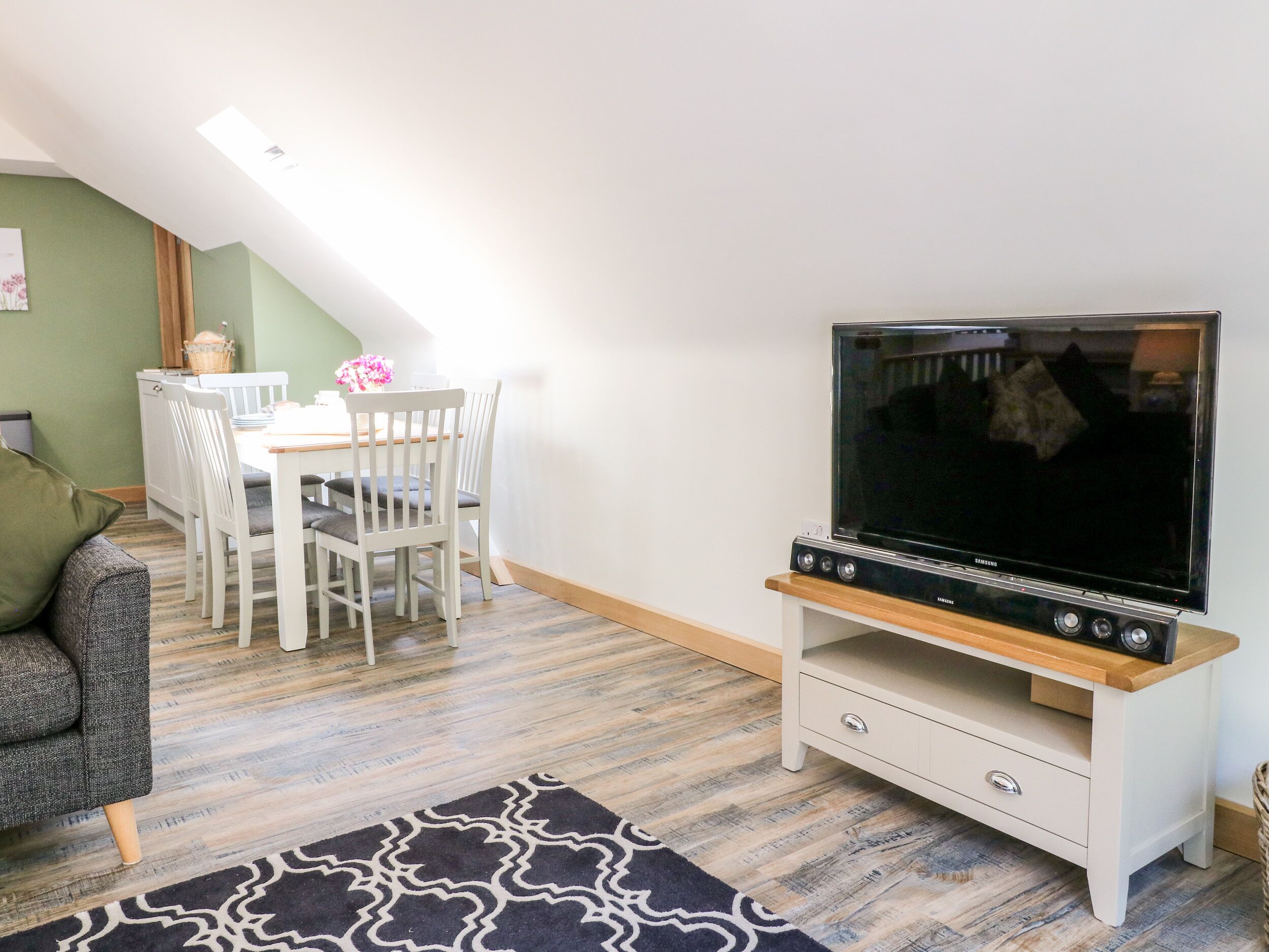 Una stanza accogliente con un tavolo da pranzo, sedie, una TV su un mobile, un divano e un tappeto decorato.