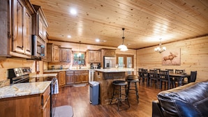 A spacious kitchen with wooden cabinets, a central island, and a dining area with a table and chairs. - Luxury Broken Bow Lodge | 7 King Suites | Sleeps 20+ (Broken Bow)