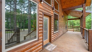 A wooden log cabin with large windows, a covered porch, and a welcome mat. - Luxury Broken Bow Lodge | 7 King Suites | Sleeps 20+ (Broken Bow)