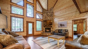 A log cabin interior with a stone fireplace, leather sofas, and large windows. - Luxury Broken Bow Lodge | 7 King Suites | Sleeps 20+ (Broken Bow)