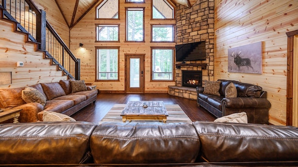 A log cabin interior with a fireplace, leather sofas, a wooden coffee table, and a stone fireplace surround. - Luxury Broken Bow Lodge | 7 King Suites | Sleeps 20+ (Broken Bow)