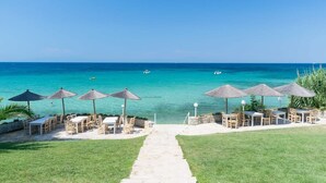 Un complexe hôtelier situé en bord de mer, doté d’une terrasse avec des parasols, offrant une vue dégagée sur l’océan et un sentier menant à la plage.