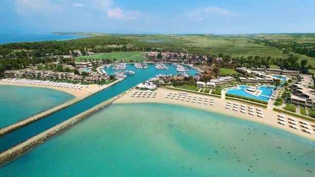 Vue aérienne d’une station balnéaire dotée de plusieurs piscines, d’un port de plaisance et d’hébergements situés en bord de mer.