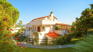 Une villa moderne avec un toit recouvert de tuiles rouges, entourée d’une végétation luxuriante et de plantes en fleurs.