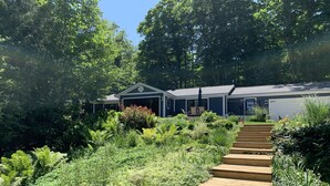 Une maison dotée d’un porche abrité, d’un garage et d’un jardin bien entretenu, avec un escalier en bois menant à la porte d’entrée.