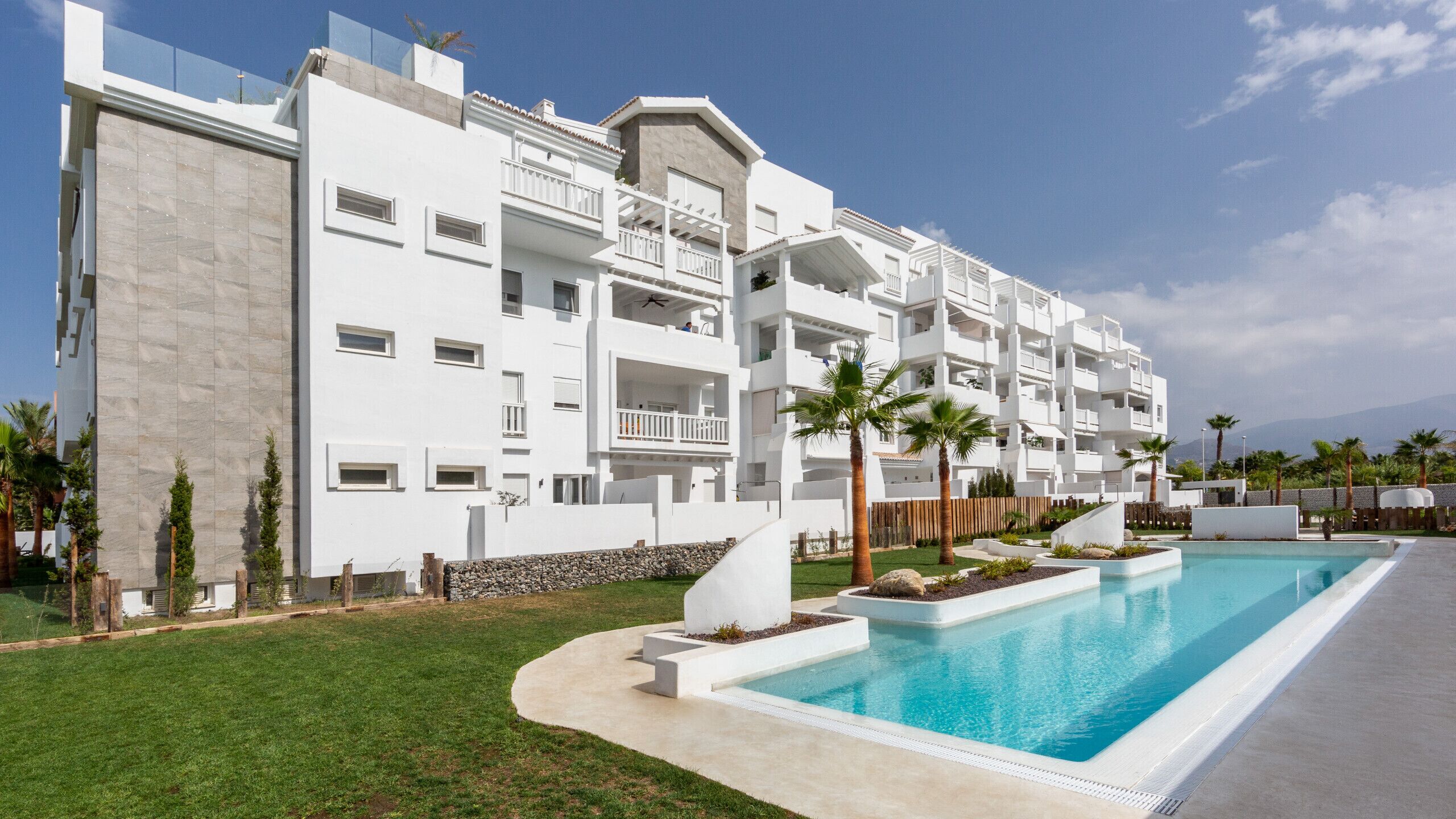 Un hotel moderno con piscina, fachada blanca y balcones.