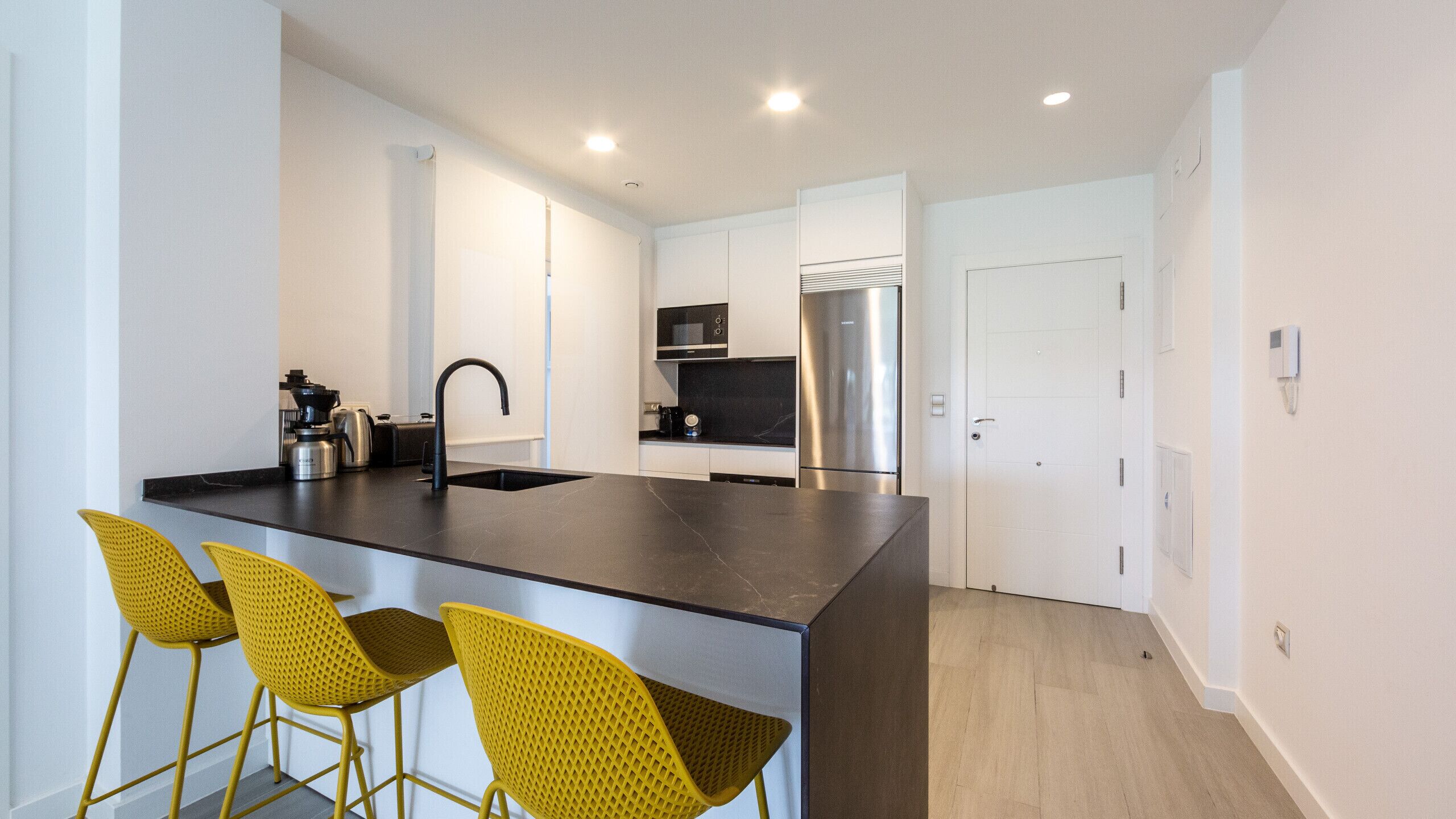 A modern kitchen with a central island, stainless steel appliances, and yellow chairs.