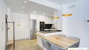 A modern kitchen with white cabinetry, stainless steel appliances, and a wooden dining table with grey chairs.