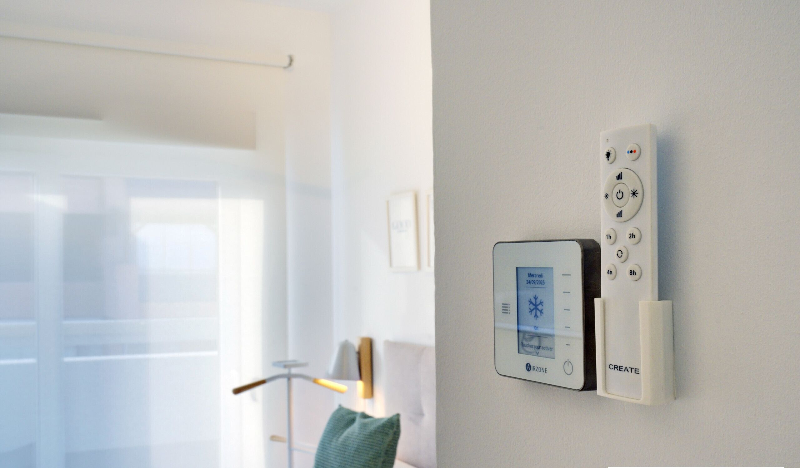 Termostato y control remoto montados en una pared en una habitación moderna con una ventana, una lámpara de pie y un cojín verde.