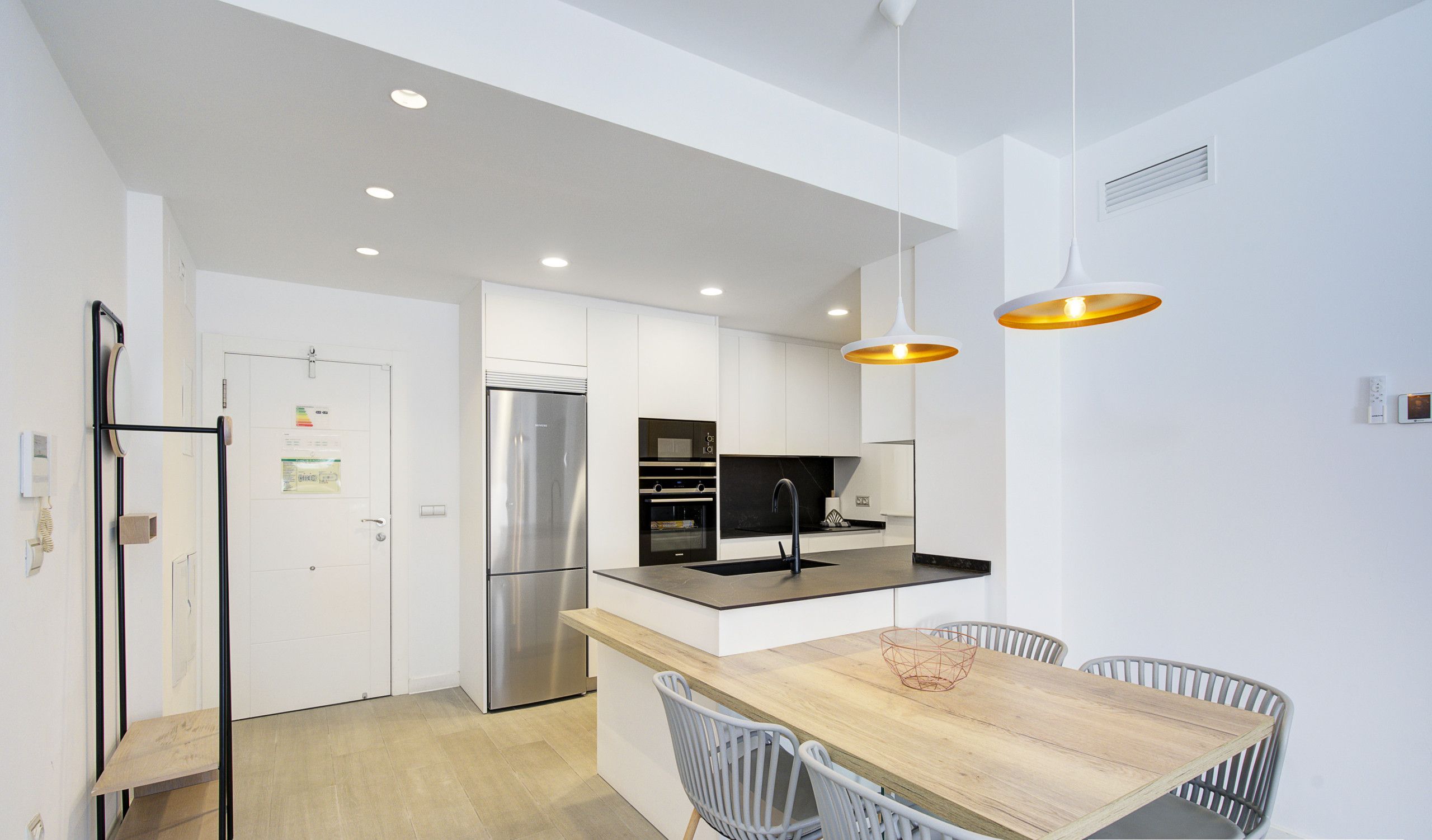 Una cocina moderna con armarios blancos, electrodomésticos de acero inoxidable y una mesa de comedor de madera con sillas grises.