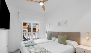 A hotel room with two beds, a ceiling fan, a TV, and a balcony with a view of buildings. - Ref. 336891 (Motril)