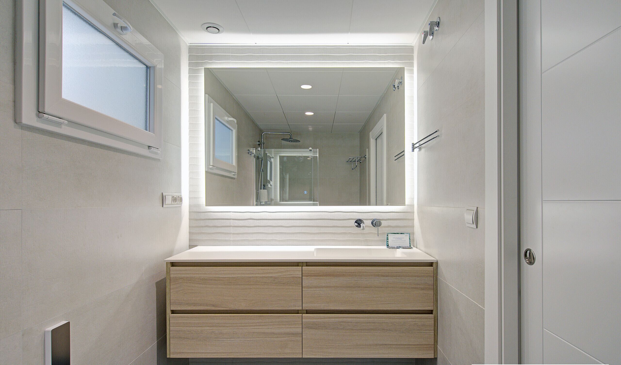 Un baño moderno con un espejo grande, un lavamanos y una ducha.