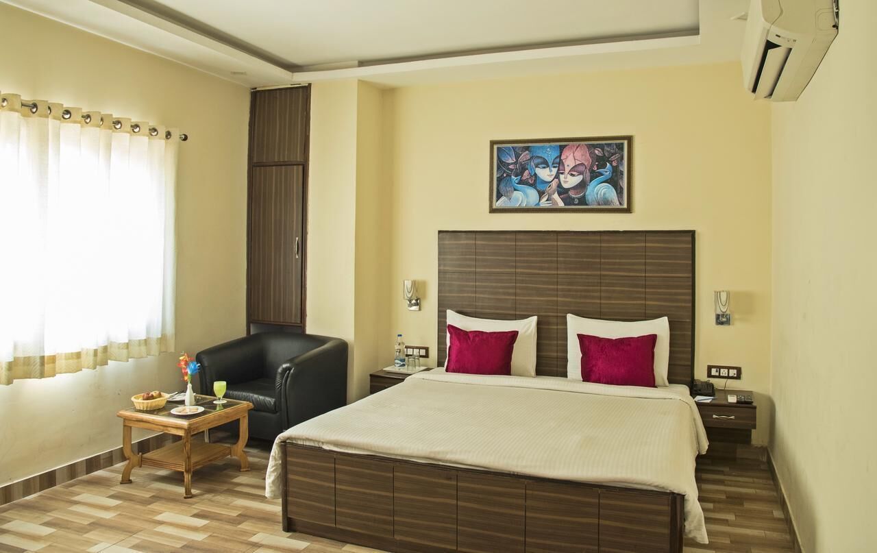 A hotel room with a bed, a chair, a small table, and a painting on the wall.