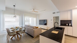 A modern kitchen with a black countertop, a dining area with a glass table and wooden chairs, and a grey sofa. - Ref. 338306 (Motril)