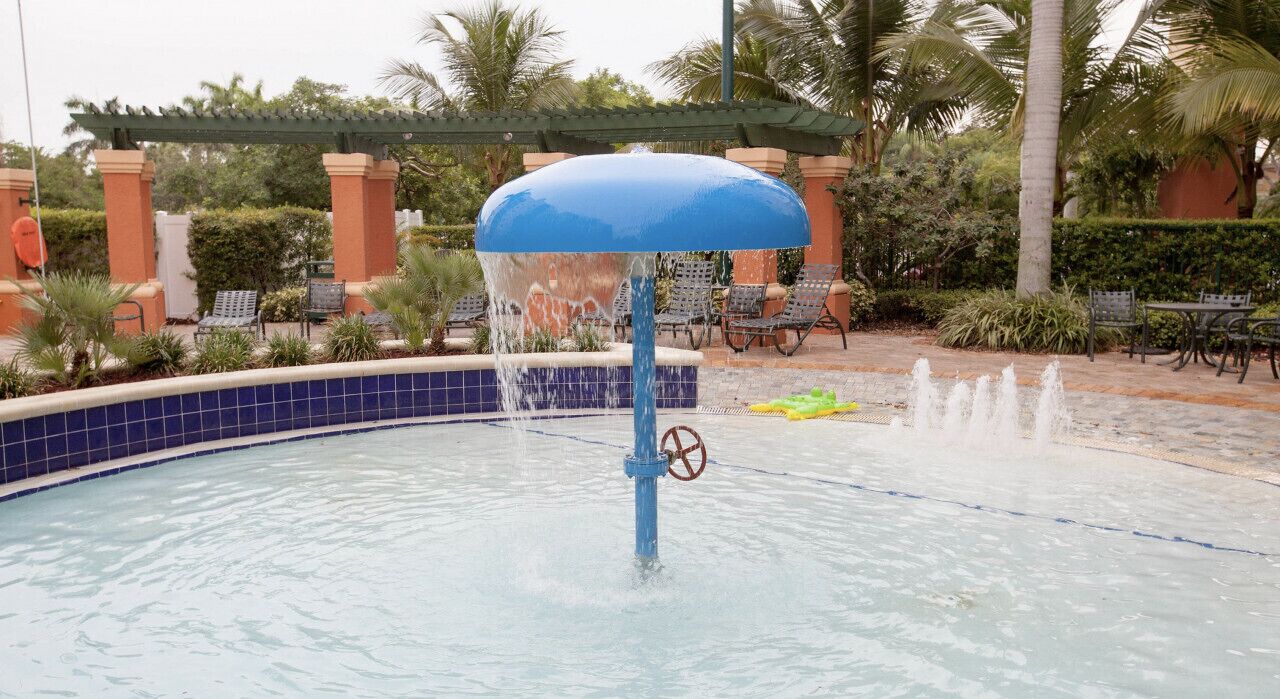 A pool with a blue umbrella, water jets, and lounge chairs.