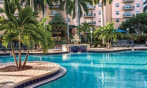 A swimming pool with lounge chairs and palm trees, surrounded by a building with balconies. - Official Wyndham Palm-Aire 2BR Suite - Sleeps 8 - Pools, Balcony & Resort Access (Pompano Beach)