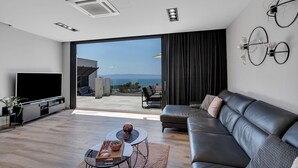 A modern living room with a flat-screen TV, leather sofa, and a dining area with a table and chairs.