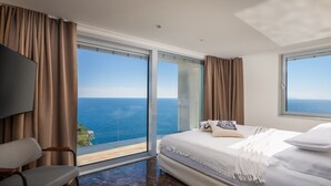 Ein Hotelzimmer mit großem Fenster und Meerblick, einem Bett mit weißer Bettwäsche und einem modernen Sessel.