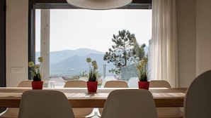 A dining area with a view of mountains and a tree, featuring a wooden table and white chairs.