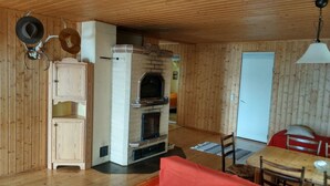 A cozy room with a fireplace, wooden walls, a dining table, and a red chair. - Lomakoti kauniilla näkymillä Saimaan rannalla (Savonlinna)