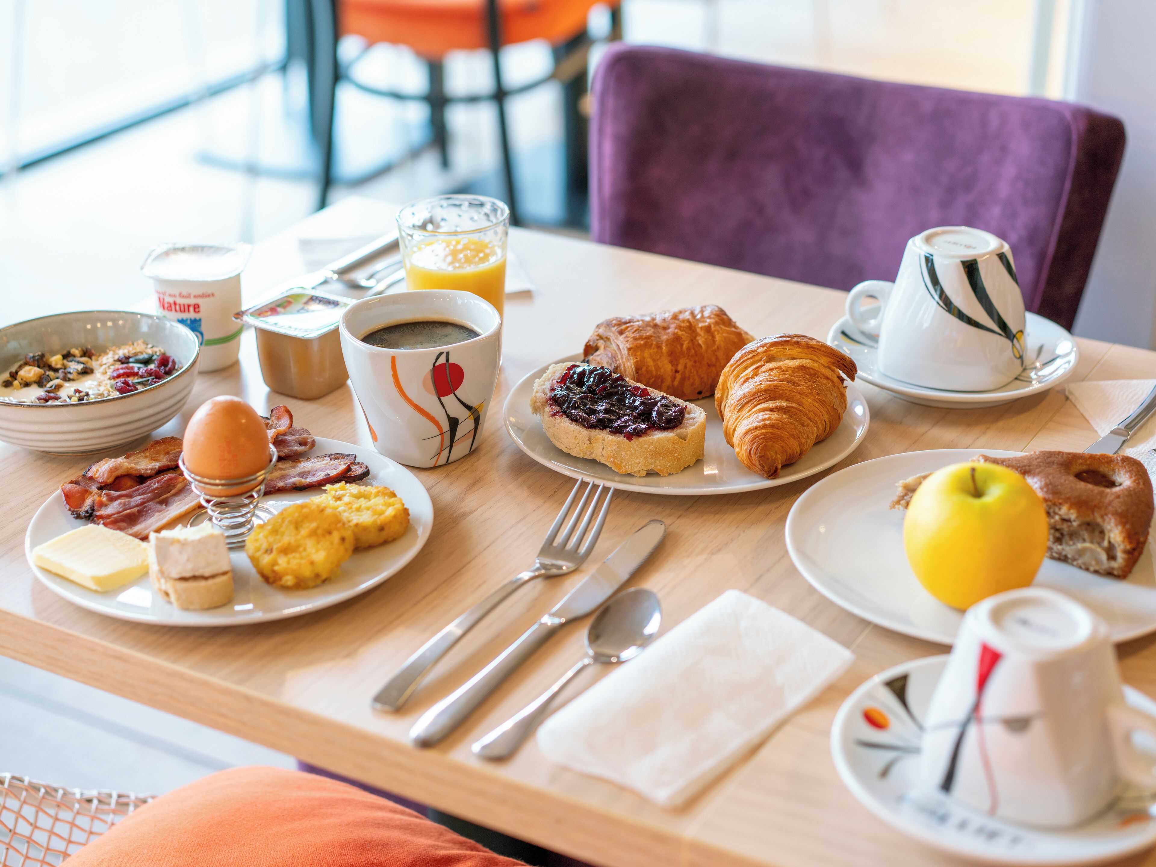 Una mesa de desayuno con platos de comida, una taza de café y un croissant.