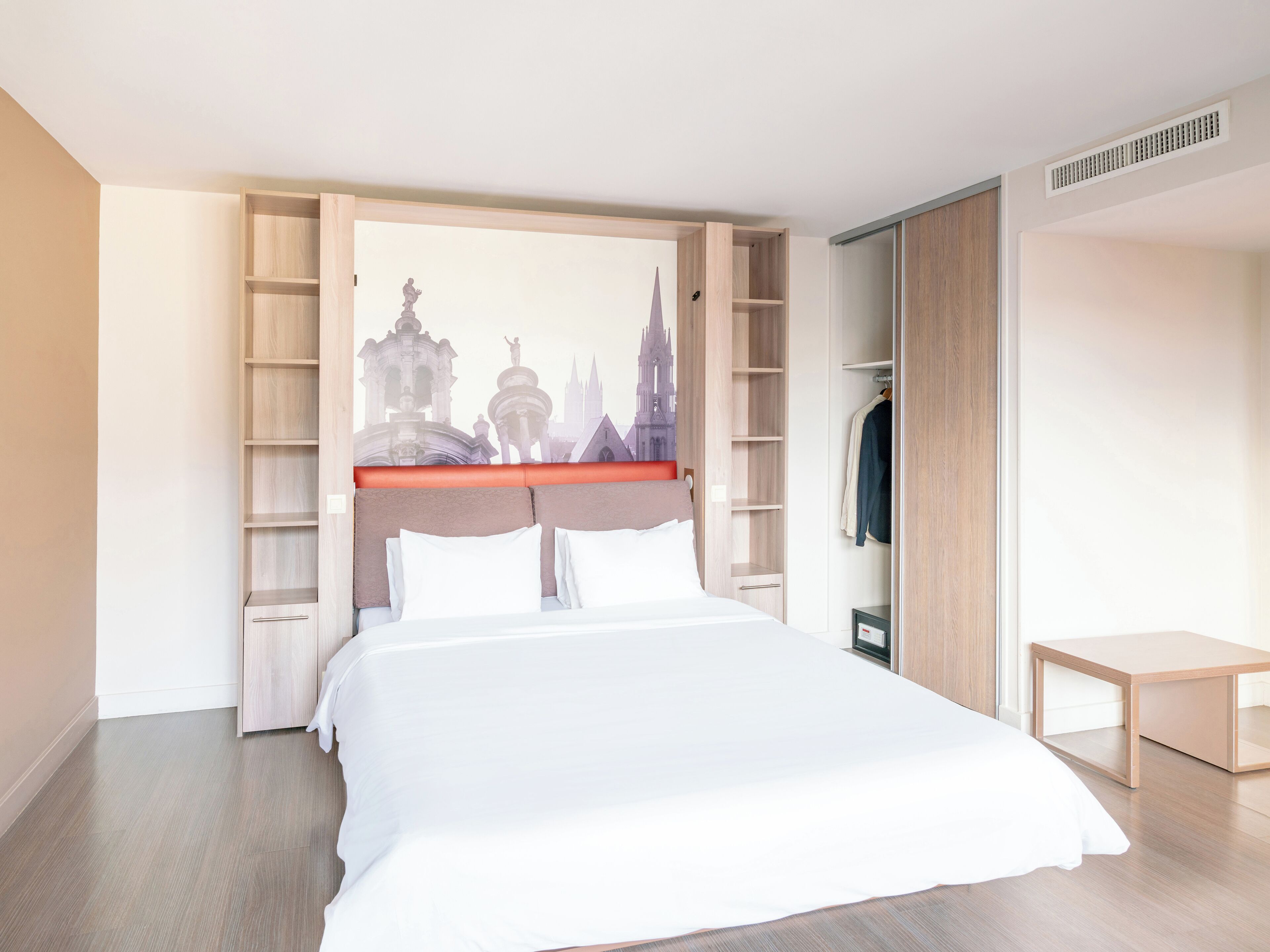 A hotel room with a bed, a wardrobe, and a small table.