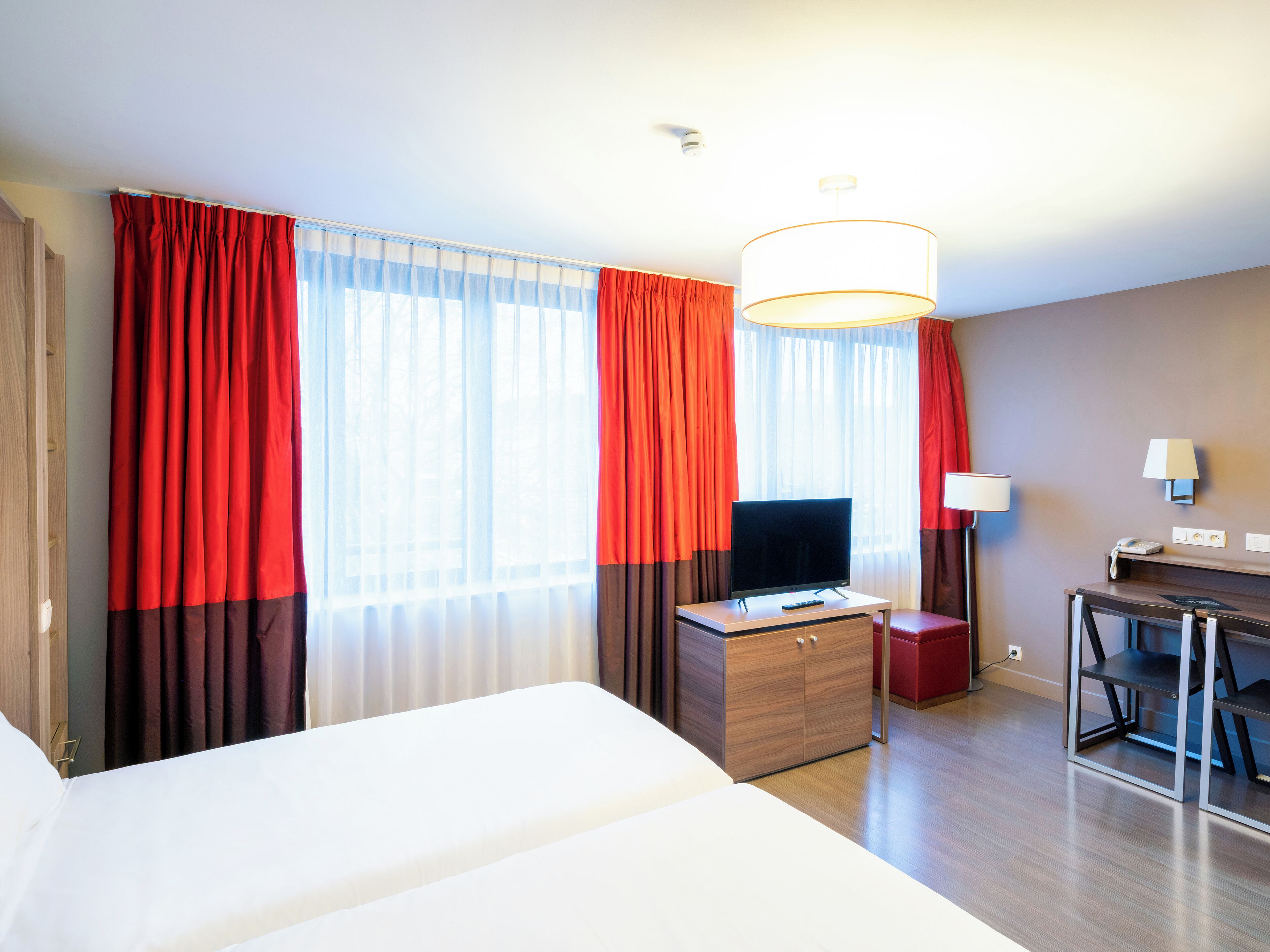 A hotel room with a large bed, a desk with a television, and a desk lamp.