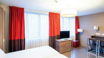 A hotel room with a large bed, a desk with a television, and a desk lamp.