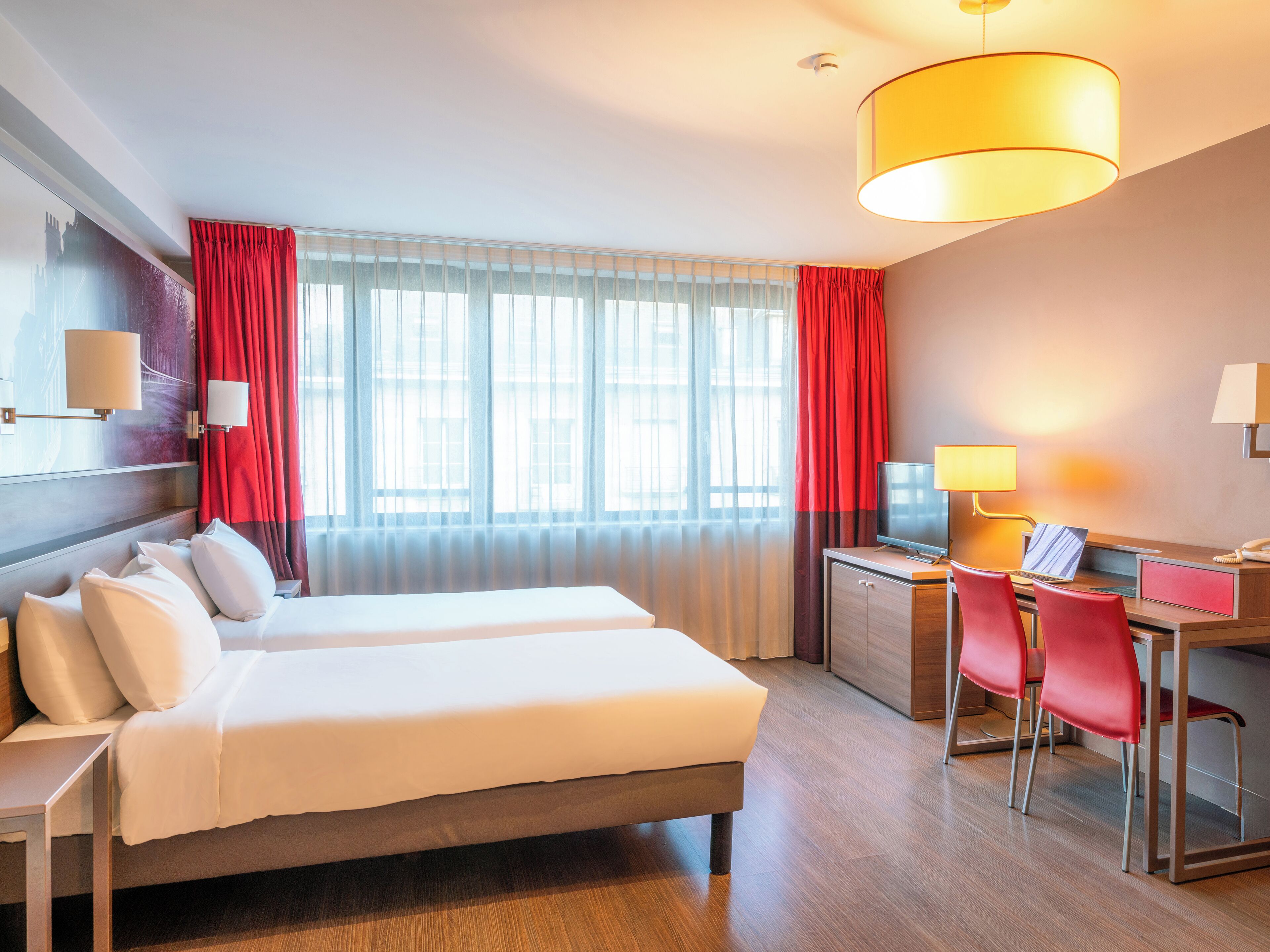 A hotel room with two beds, a desk with a computer, a TV, and a lamp.