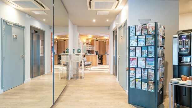 A modern hotel lobby with a reception desk, a coffee machine, and a magazine rack. - B&B HOME Caen Centre Gare (Caen)