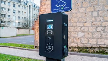 An electric vehicle charging station with a digital display, a charging point symbol, and a nearby sign indicating it is a public charging point.